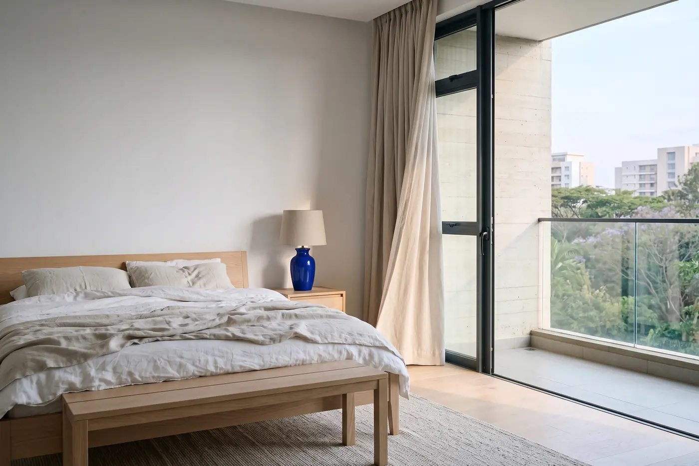 A principal bedroom with a low oak bed, linen curtains and a door to the balcony