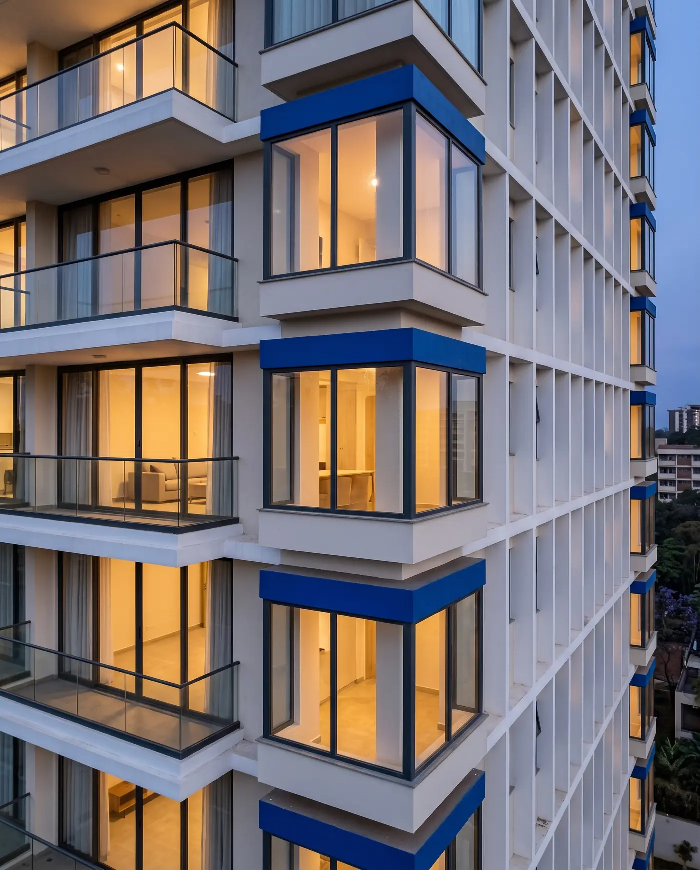 Three corner bays stacked up the building at dusk, lit from inside, each under a deep cobalt band