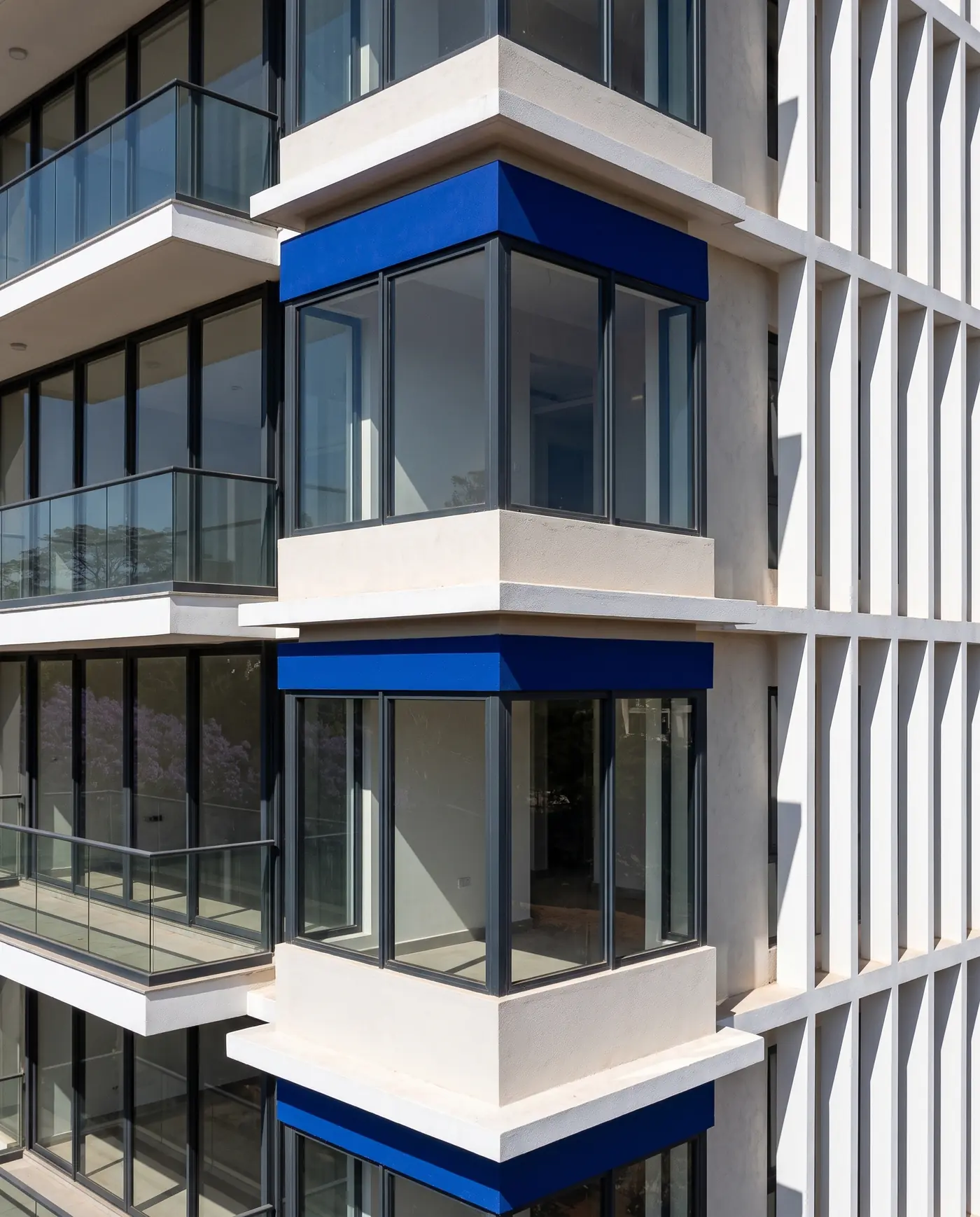 A corner bay in bright sun, its cobalt band casting a shadow on the glass, beside the deep white fins of the side façade